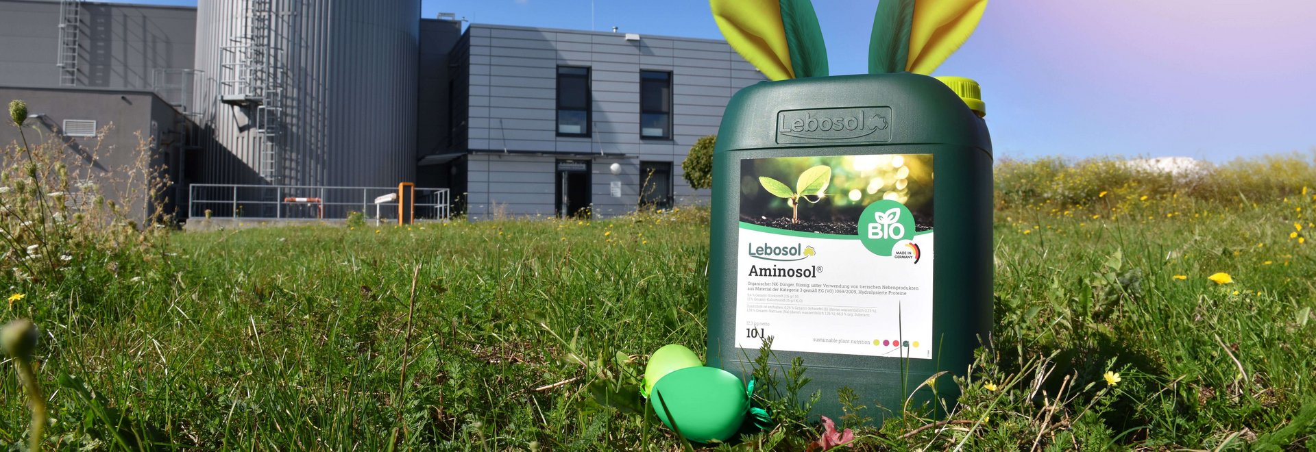 Ein grüner 10 Liter Kanister von Lebosol® mit Aminosol® Etikette steht auf einer grünen Wiese vor einem Gebäude. Der Kanister hat Hasenohren
