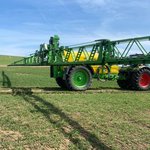 Traktor mit Spritzarmen der über ein Getreidefeld fährt