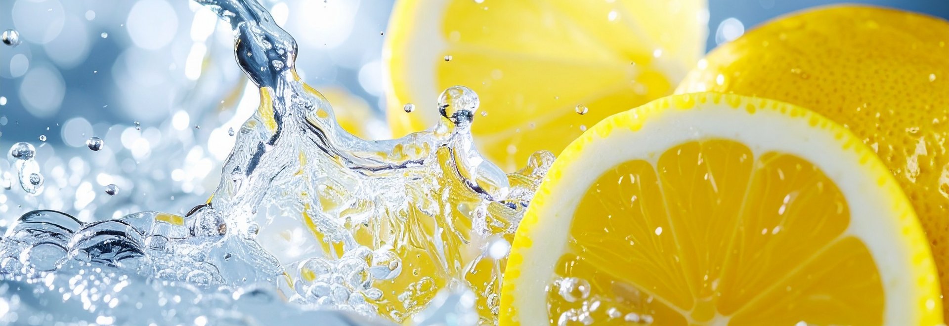 Gelbe Zitronenscheiben die in klares Wasser fallen.