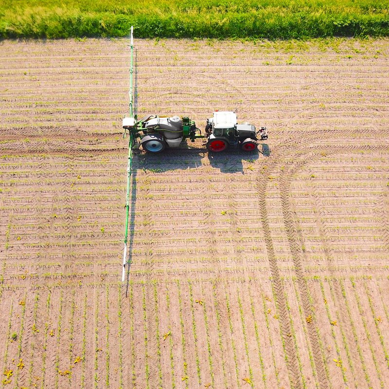 Traktor mit Spritzarm fährt über Feld.