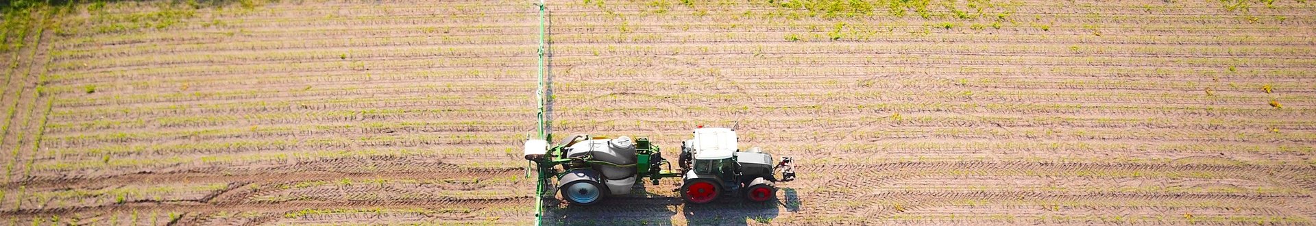 Traktor mit Spritzarm fährt über Feld.