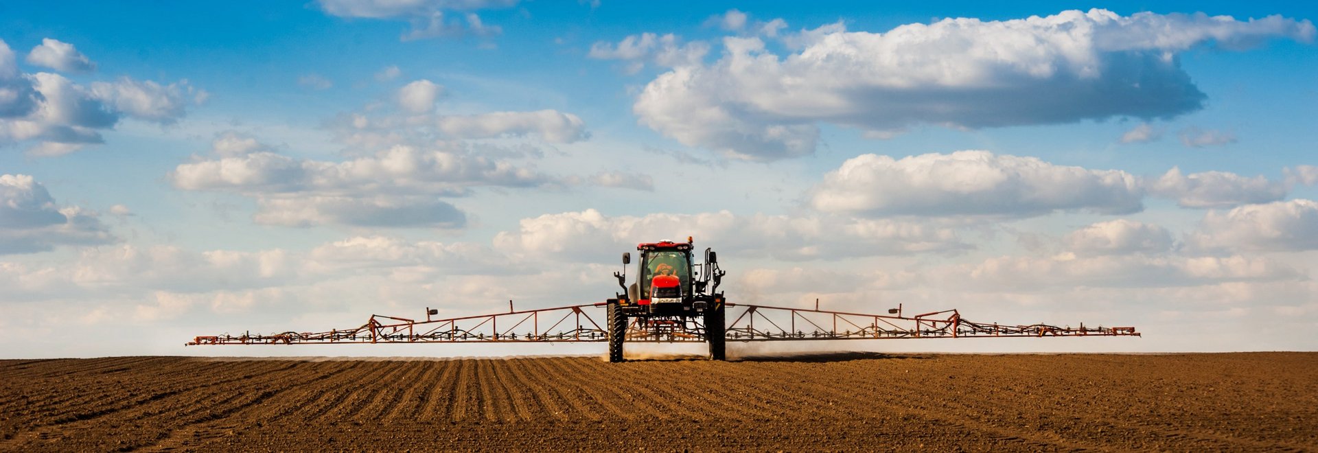 Traktor mit Spritzarm fährt über Feld.