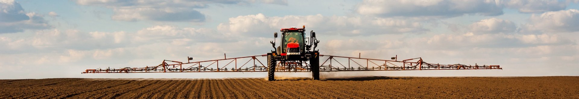 Traktor mit Spritzarm fährt über Feld.