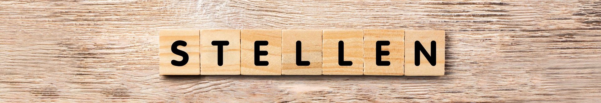 Holzhintergrund mit Würfel auf denen Buchstaben stehen welche das Wort Stellen ergeben