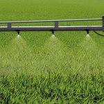 Spritzdüsen an einem Traktor der über ein grünes Feld fährt und Düngemittel spritzt