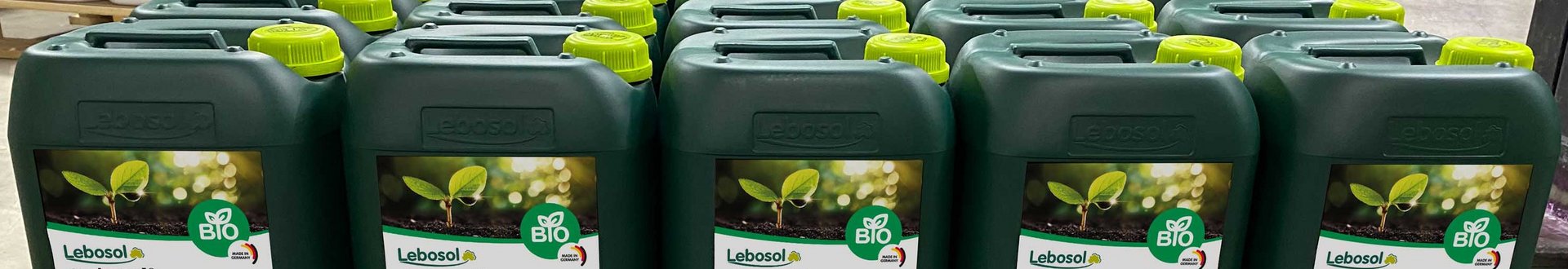 Eine Reihe von 10 Liter dunkelgrünen Kanistern Aminosol® auf einer Holzpalette