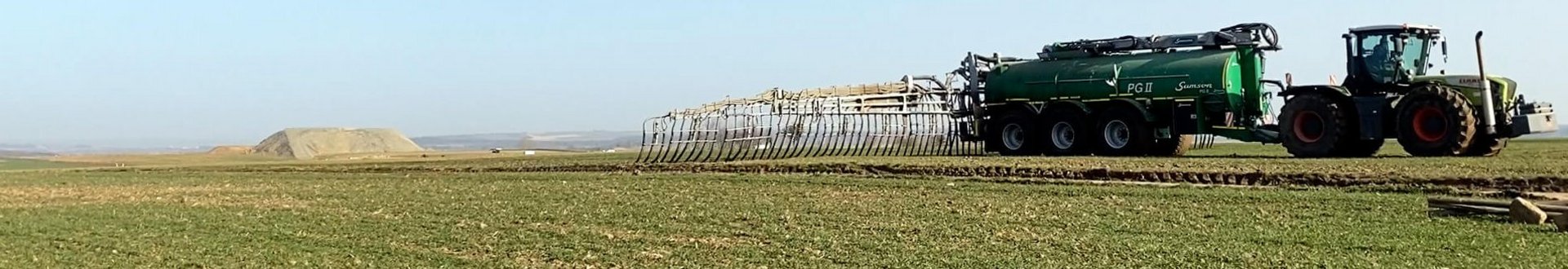 Traktor fährt über ein Feld mit kleinen Pflanzen und bringt Gülle aus