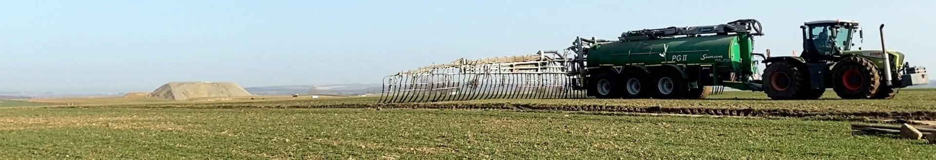 Traktor fährt über ein Feld mit kleinen Pflanzen und bringt Gülle aus