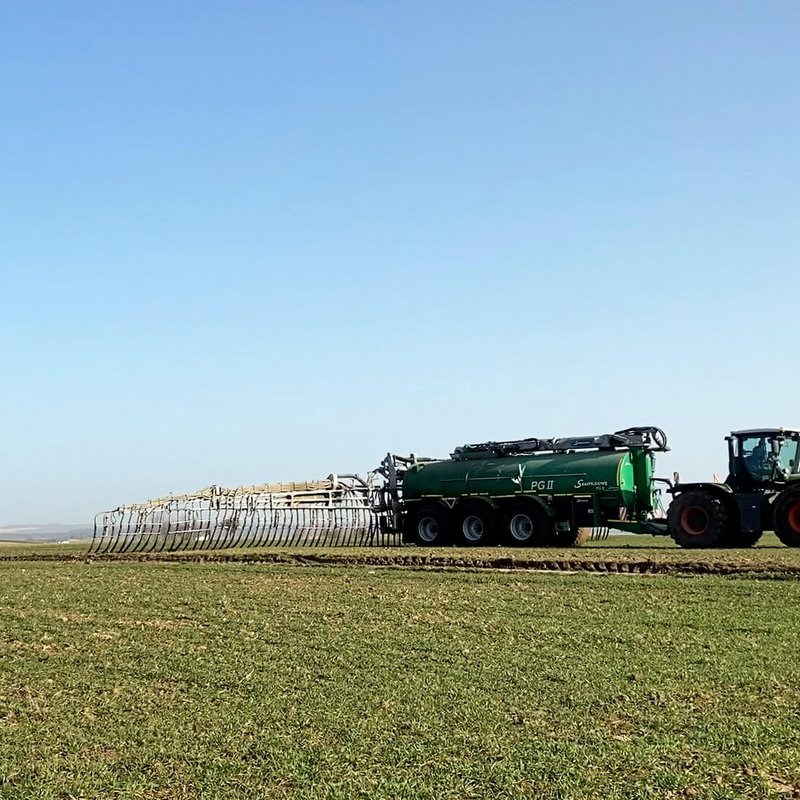 Traktor fährt über ein Feld mit kleinen Pflanzen und bringt Gülle aus
