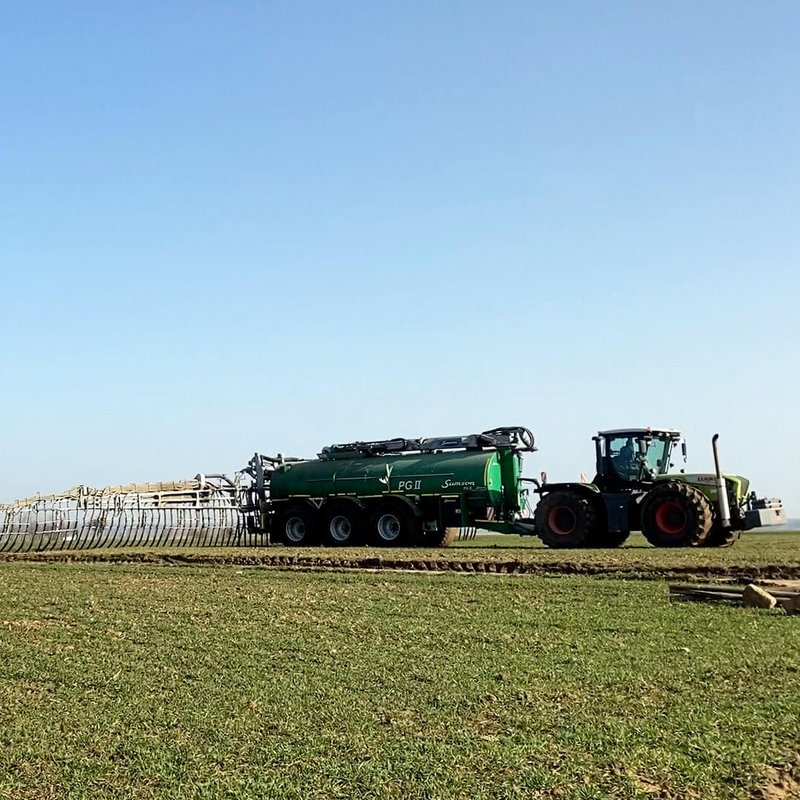 Traktor fährt über ein Feld mit kleinen Pflanzen und bringt Gülle aus