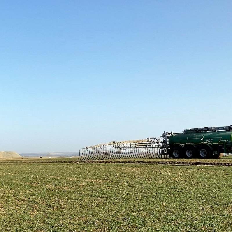 Traktor fährt über ein Feld mit kleinen Pflanzen und bringt Gülle aus