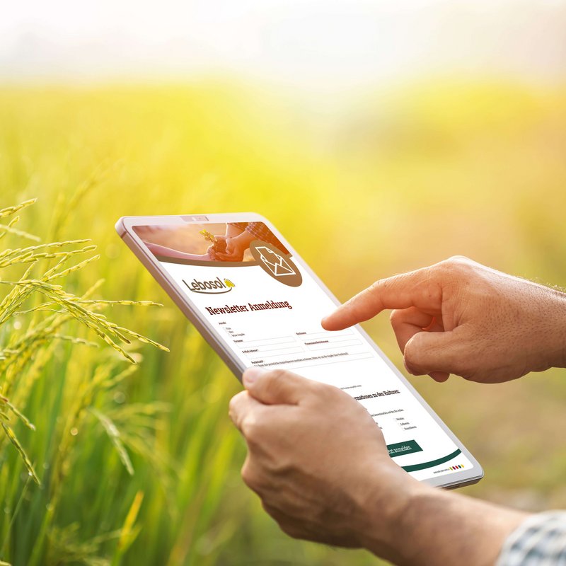 Ein Man hält auf einem Getreidefeld ein Tablet in der Hand auf der die Anmeldung zum Lebosol Newsletter zu sehen ist.
